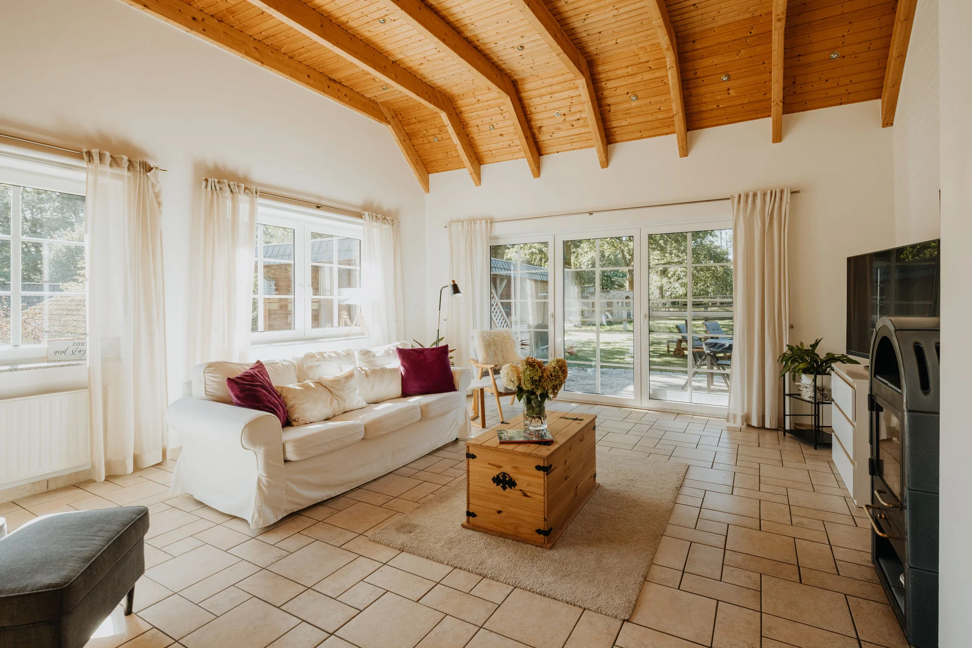 Wohnzimmer mit hellem Sofa, Holzbalkendecke und verglastem Gartenzugang in der Ferienwohnung Haverbecker Heide