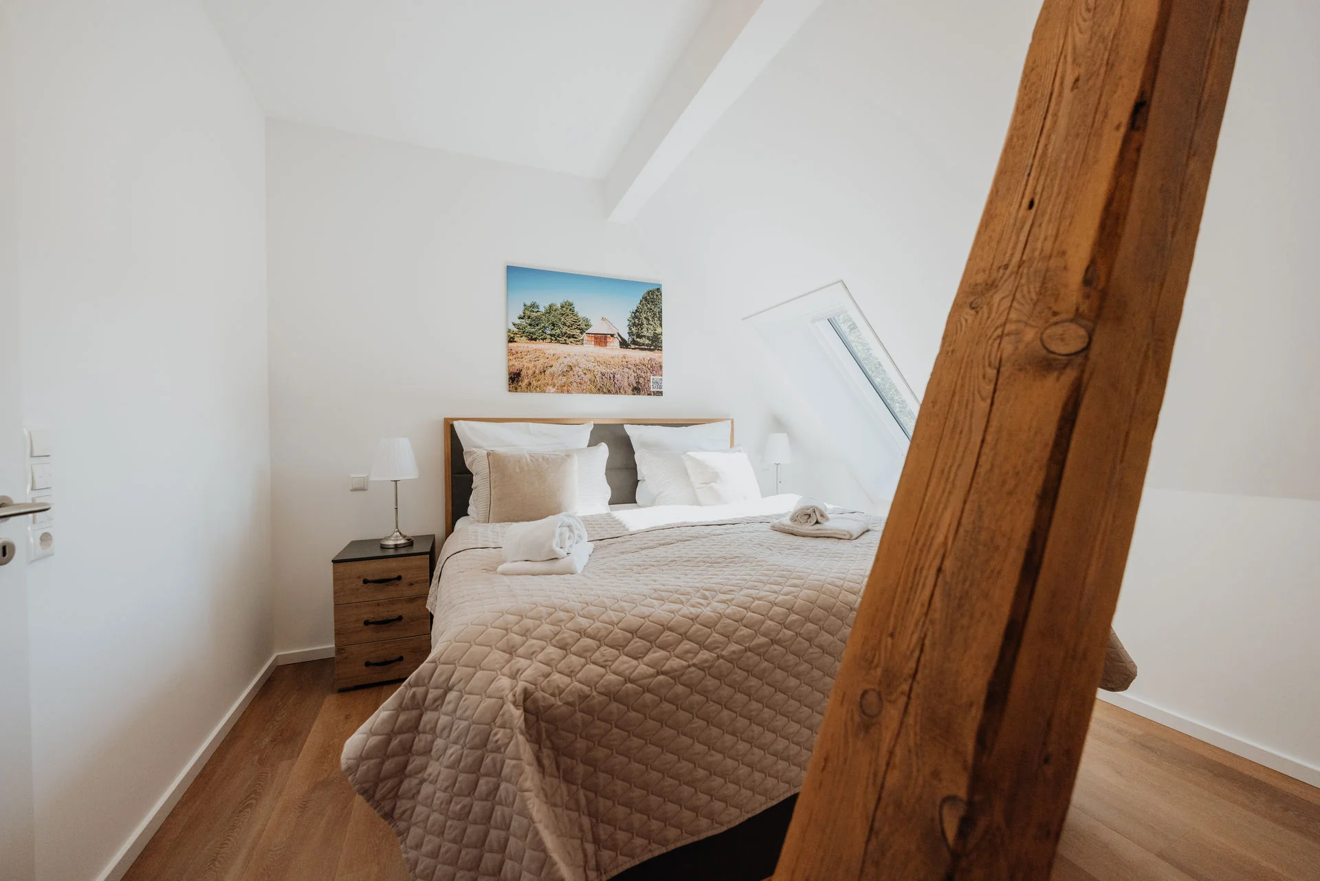 Koppelidyll: Schlafzimmer mit Doppelbett und Holzbalken im Vordergrund